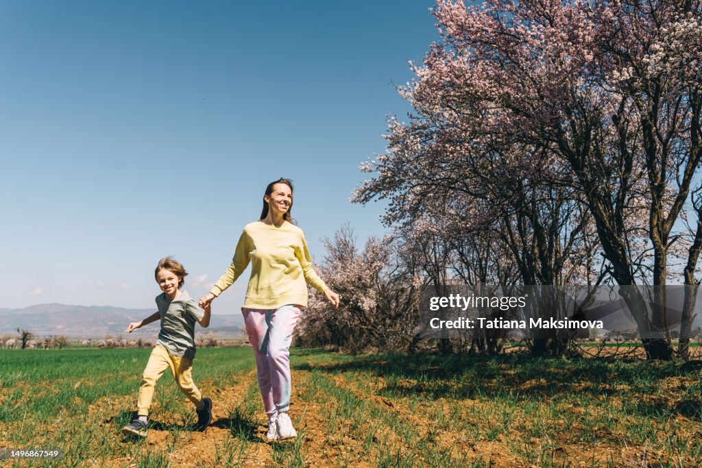 Mother and son run in the field, blossom trees around.
