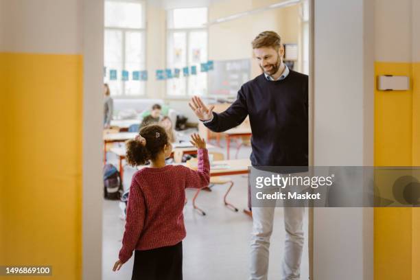 happy male teacher giving high-five to schoolgirl at doorway in school - male teacher in a classroom stock-fotos und bilder