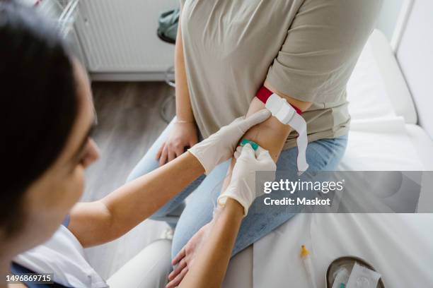 doctor wearing glove piercing needle in patient's arm at clinic - sangre fotografías e imágenes de stock