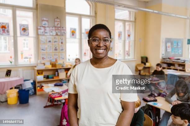 portrait of smiling teacher standing in front of students at classroom - teacher school supplies stock pictures, royalty-free photos & images