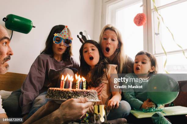man holding birthday cake with burning candles in front of surprised family at home - candeline-di-compleanno foto e immagini stock