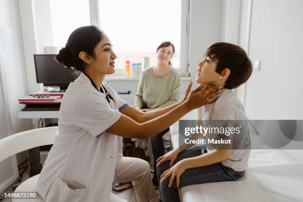 female pediatrician examining neck of boy in examination room at hospital - medical examination room stockfoto's en -beelden
