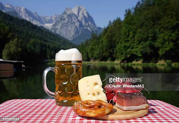 germany, upper bavaria, bavarian snacks on table, mountain with lake in background - bierkrug stock-fotos und bilder