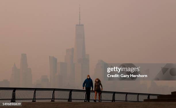 People wearing masks walk along the Hudson River as smoke shrouds the skyline of lower Manhattan and One World Trade Center as the sun rises in New...