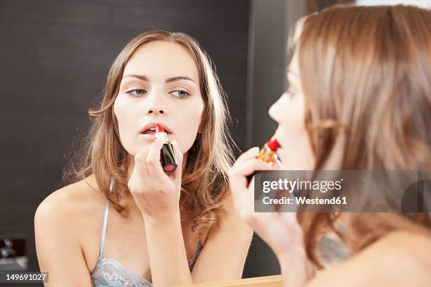 germany, bavaria, young woman applying red lipstick in bathroom - makeup and clothes stock-fotos und bilder