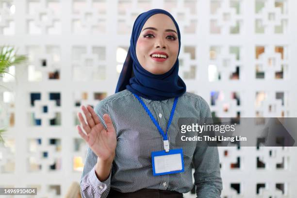front view of an asian muslim businesswoman working in a modern office space, engaging in a video conference with her business partners on a computer while speaking in front of the webcam - financial advisor virtual stock pictures, royalty-free photos & images