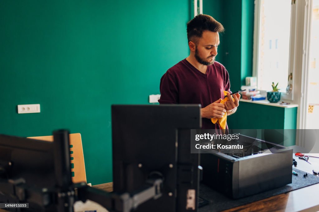 A focused millennial man uses a rag to clean the SSD part of the computer