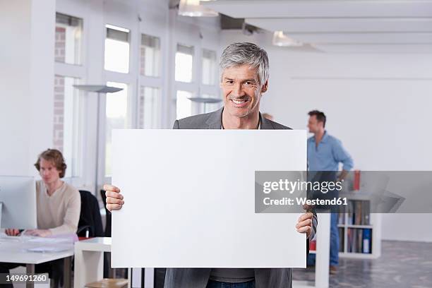 germany, bavaria, munich, mature man holding placard in office - office holding sign stockfoto's en -beelden