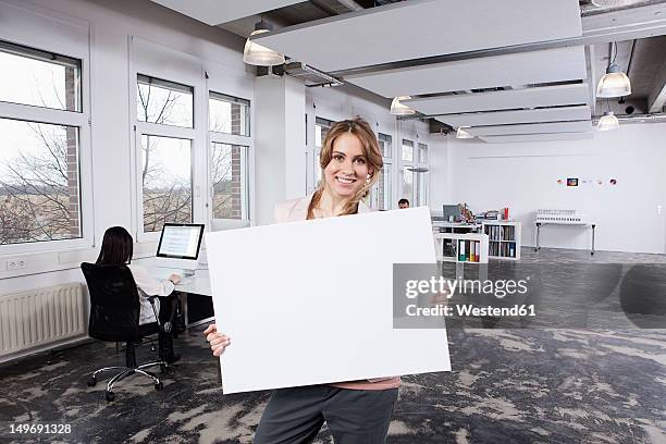 germany, bavaria, munich, woman holding placard, colleagues working in background - frau mit plakat stock-fotos und bilder