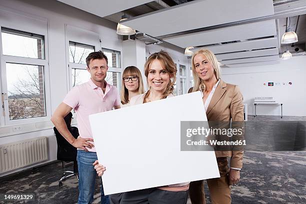 germany, bavaria, munich, young woman holding placard with colleagues in office - holding sign stock-fotos und bilder