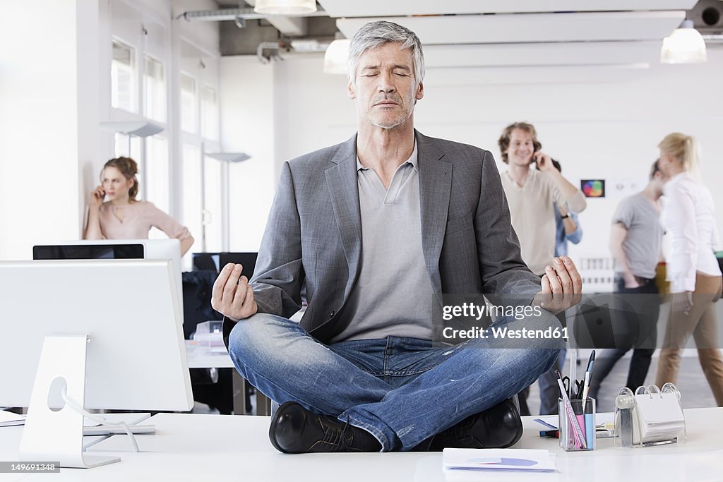 Germany, Bavaria, Munich, Man sitting in lotus position, colleagues in background