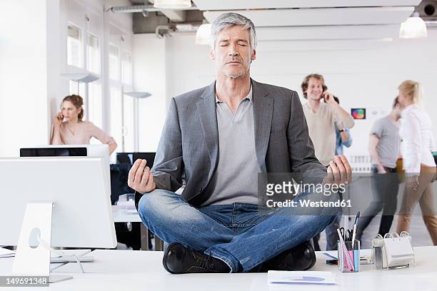 germany, bavaria, munich, man sitting in lotus position, colleagues in background - escaping office stock pictures, royalty-free photos & images