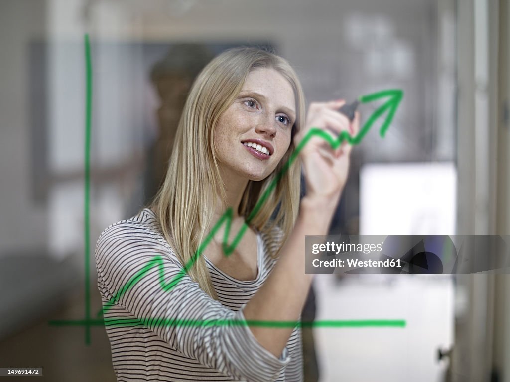 Germany, Cologne, Young woman drawing graph on glass