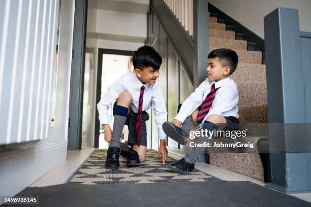 schoolboys in uniform putting on shoes in family home - aankleden stockfoto's en -beelden