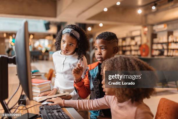 three young black readers using a computer in a library - elementary school stock pictures, royalty-free photos & images