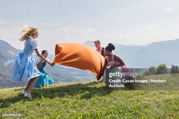teenage friends spreading picnic blanket on grass landscape, bavaria, germany - dirndl stock pictures, royalty-free photos & images