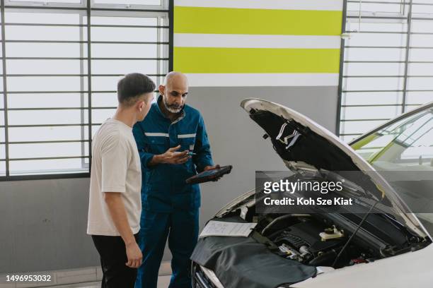 asian indian car mechanic explains and shares about the servicing required for the car to a young adult couple - asian couple garage car stock pictures, royalty-free photos & images