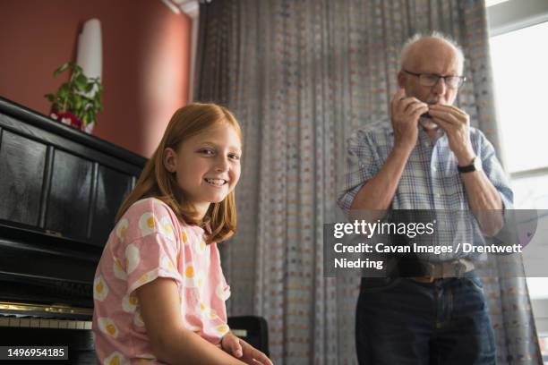 granddaughter listening while grandfather blowing harmonica instrument - harmonica stock pictures, royalty-free photos & images