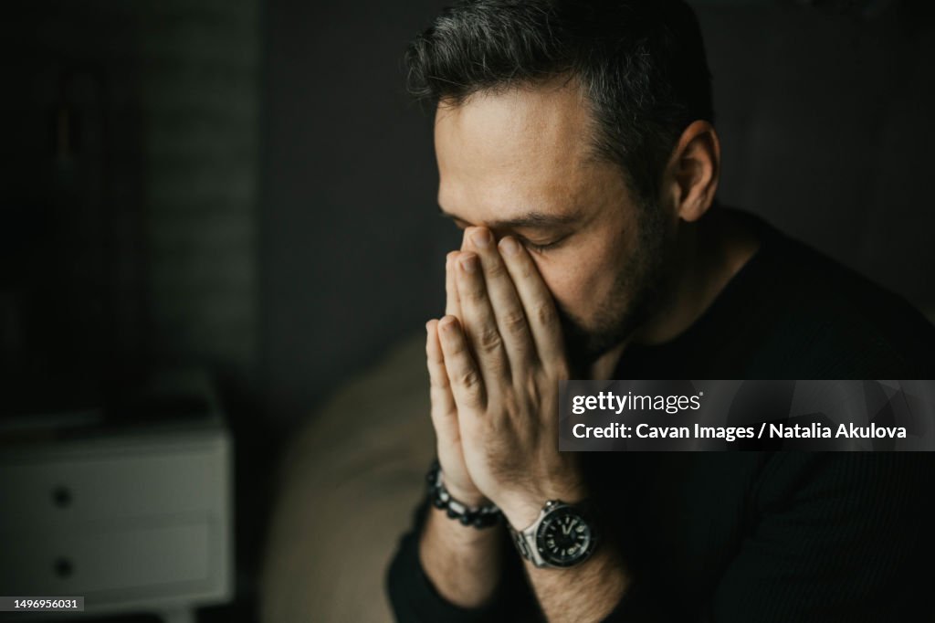 Sad man put his hands to his face sitting on the bed