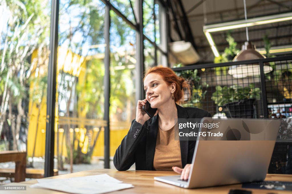 Happy young businesswoman talking on mobile phone and looking away at office