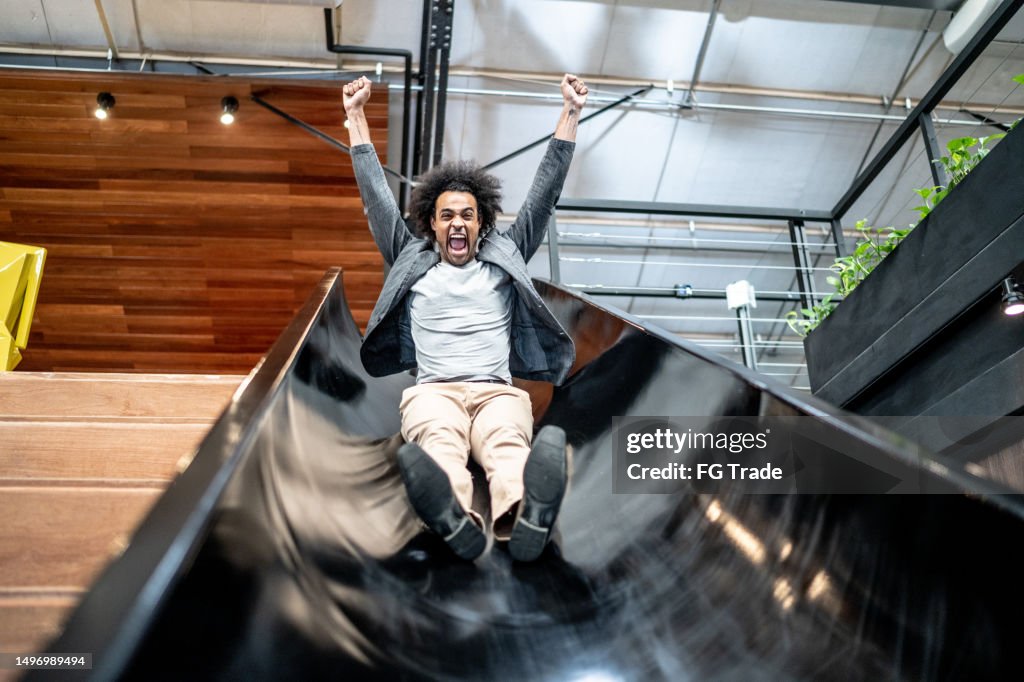 Young business man sliding down slide at coworking/office