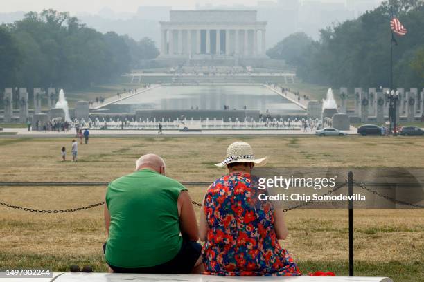 Tourists sit on benches at the base of the Washington Monument as wildfire smoke puts a veil of haze in front of the Lincoln Memorial along the...