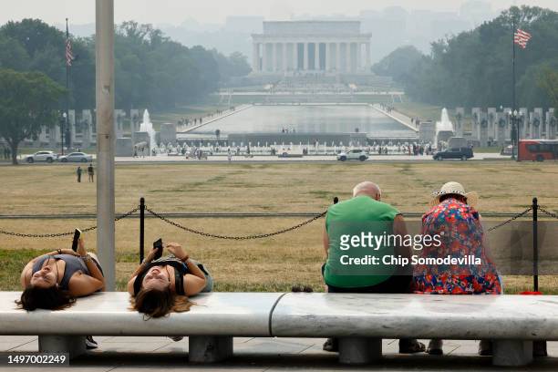 Tourists sit on benches at the base of the Washington Monument as wildfire smoke puts a veil of haze in front of the Lincoln Memorial along the...