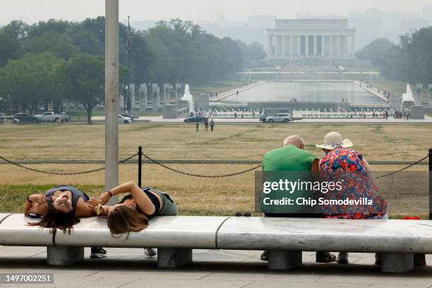 Tourists sit on benches at the base of the Washington Monument as wildfire smoke puts a veil of haze in front of the Lincoln Memorial along the...