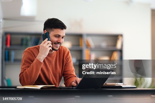 Smiling Businessman Talking On A Mobile Phone While Working On His Laptop Smiling Businessman Talking On A Mobile Phone While Working On His Laptop