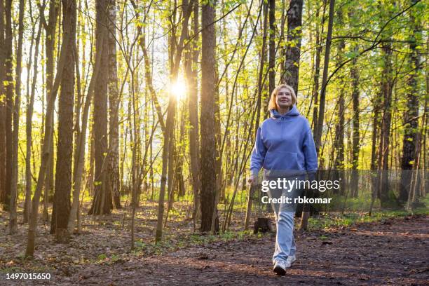 happy woman walking in sunlit park at sunset in spring - active retirement lifestyle - walking and relax stock pictures, royalty-free photos & images