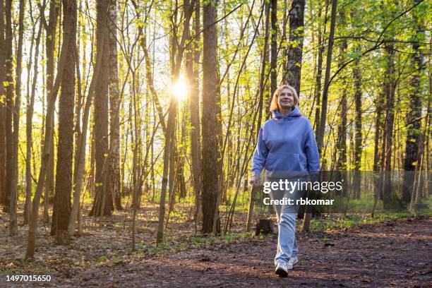 happy woman walking in sunlit park at sunset in spring - active retirement lifestyle - andar imagens e fotografias de stock