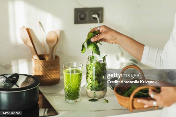 young beautiful woman making green spinach smoothie on kitchen. - spinat stock-fotos und bilder