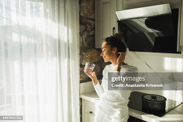 young beautiful woman drinking still water on kitchen in morning. - stoffwechsel entgiftung stock-fotos und bilder