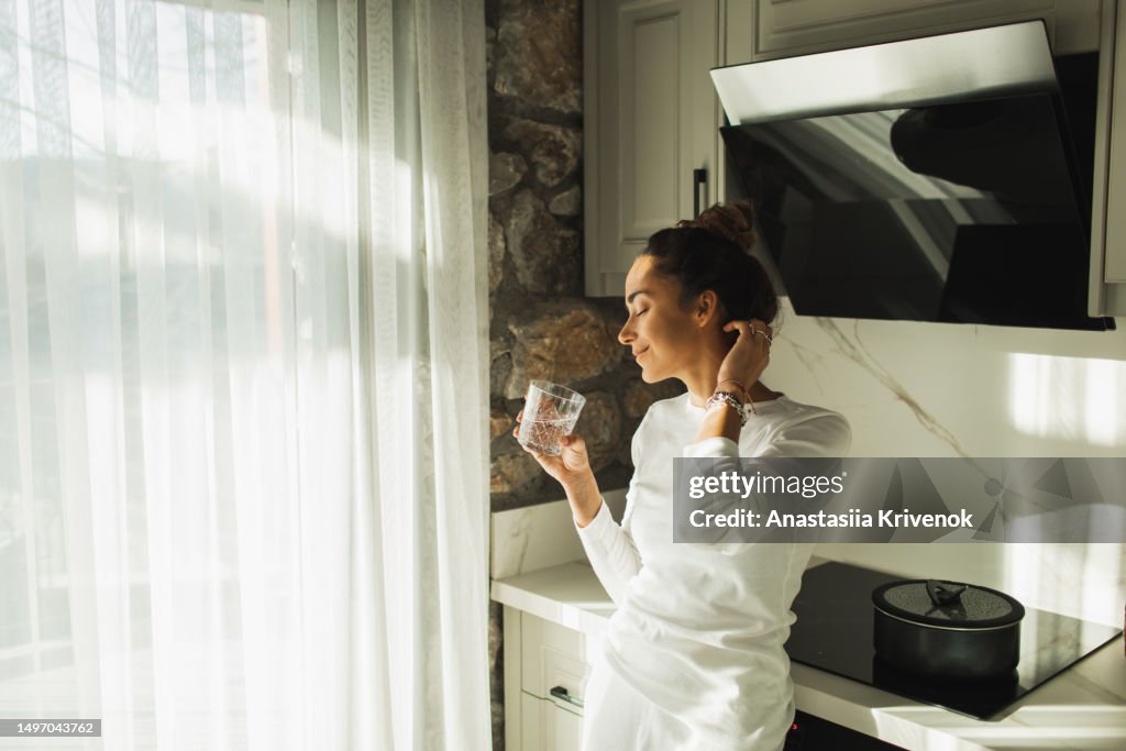 Young beautiful woman drinking still water on kitchen in morning.