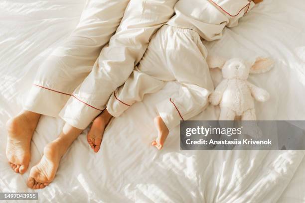 bare feet and legs of mother and little daughter in similar pajamas lying in bed. - womans bare feet fotografías e imágenes de stock