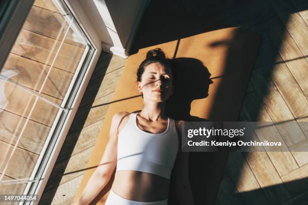 young athletic caucasian woman doing yoga while lying with her eyes closed in dead body pose. dark-haired girl wears sports top to class. rest and recovery concept - curvy white girl photos et images de collection