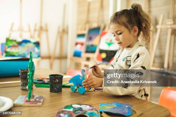 little girl coloring wooden dinosaur she made herself in kids club. - babysitters club stock pictures, royalty-free photos & images