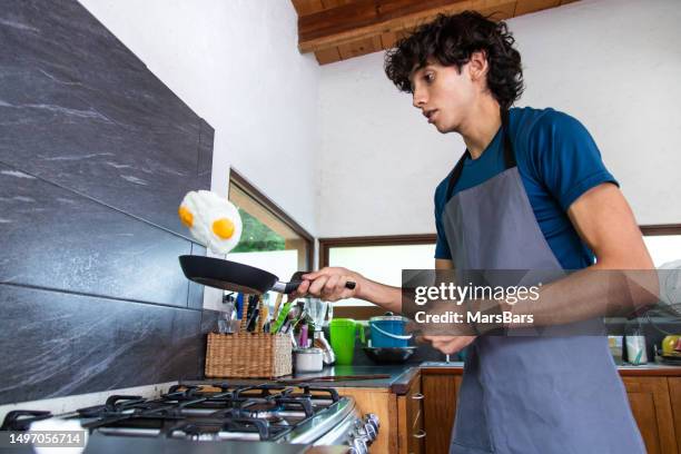 young man cooking on a gas stove range - flying egg stock pictures, royalty-free photos & images