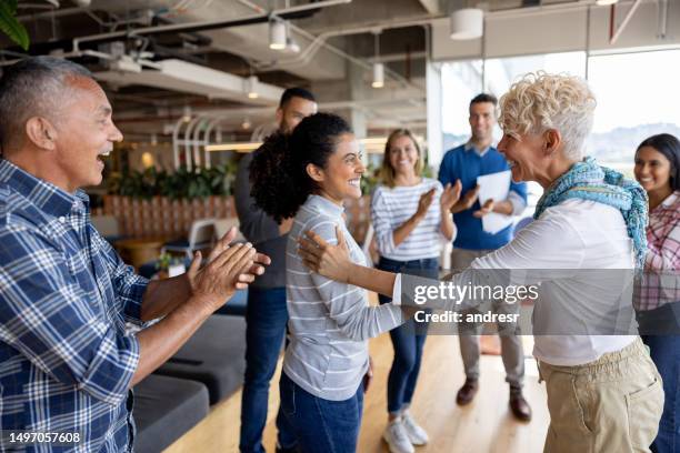 boss giving woman a promotion at the office and team clapping for her - congratulating imagens e fotografias de stock