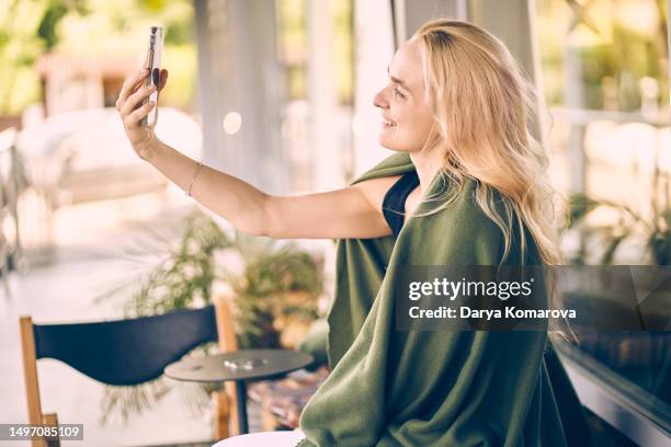 beautiful young woman using smartphone and smiling. blond woman in green blanket with copy space. - medium length hair stockfoto's en -beelden