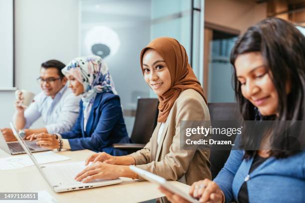 asian businesswoman with hijab, dressed in smart casual clothes working in modern corporate company. multi ethnic employees working together - smart numbers office stockfoto's en -beelden