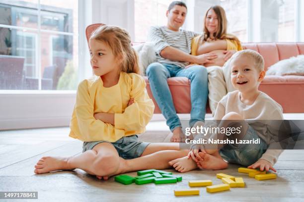 children play jenga on the floor, parents sit in the background - jenga stockfoto's en -beelden