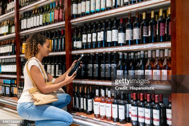 black young woman kneeling while grabbing a bottle of wine at the supermarket - argentina wine stock pictures, royalty-free photos & images
