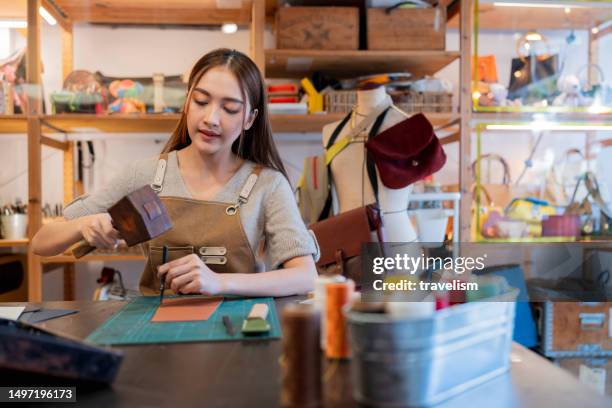 closeup leather work hands of young female leather maker using a small wooden hummer with leather punching steel to make a leather belt for customers in workplace home studio - leather craft stock pictures, royalty-free photos & images