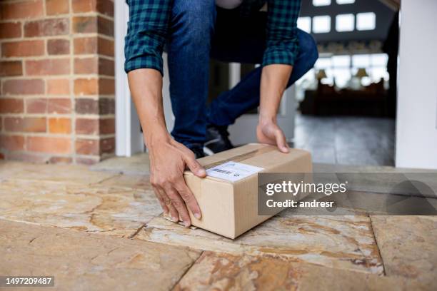 primer plano de un hombre recogiendo un paquete dejado en el porche - recibir fotografías e imágenes de stock