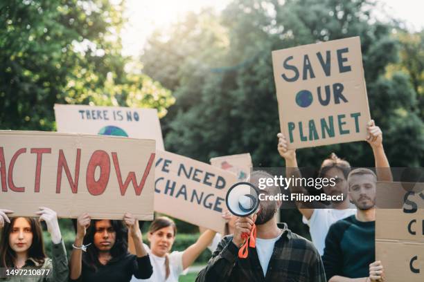 a group of climate activists are marching together holding signs - climate change stock pictures, royalty-free photos & images