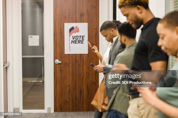 group of people stand in line at the community center waiting to vote - governments stock pictures, royalty-free photos & images