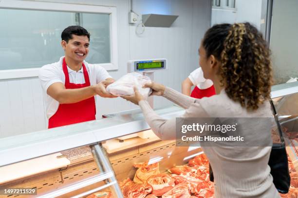 freundlicher junger mann, der in der metzgerei arbeitet und einer kundin eine tüte mit frischem fleisch überreicht - supermarket help stock-fotos und bilder