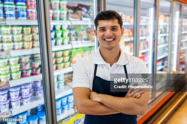 porträt eines jungen mannes, der im supermarkt im kühlregal arbeitet und mit verschränkten armen vor der kamera l�ächelt - grocer stock-fotos und bilder