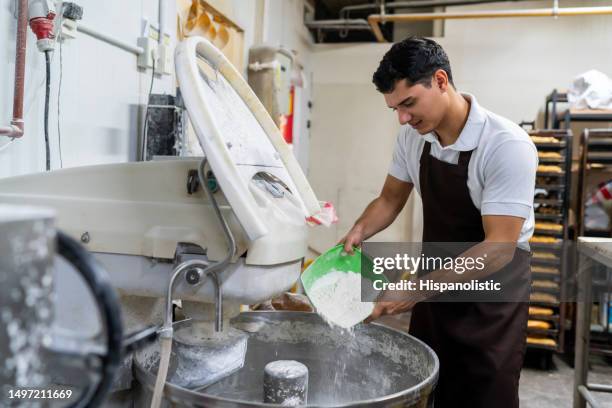 young male baker adding flour to an industrial mixer to prepare bread at a factory - electric mixer stock pictures, royalty-free photos & images